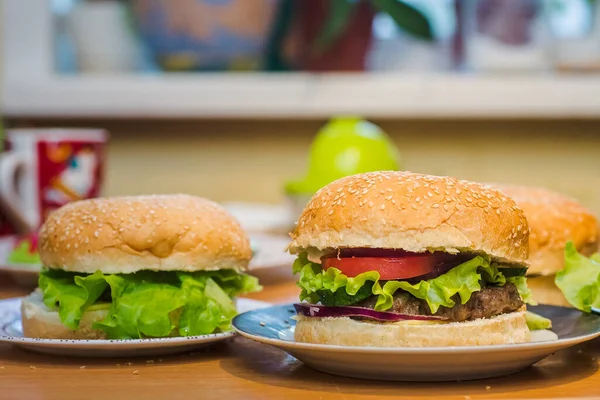 Domates ve köfteli iki ev yapımı burger, akşam yemeği için mutfak masasında tam tahıllı ekmek üzerine taze malzemeler..