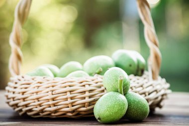 Hasır sepette yeşil ceviz. Sağlıklı yiyecekler için malzeme koleksiyonu. Eski bir masa ve olgunlaşmamış ceviz meyvesi.