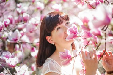 Kadının elinde pembe çiçekli manolya dalı var. İlkbaharda çiçeklenmeye alerjisi var. Mükemmel bir şişkinlik riski var..