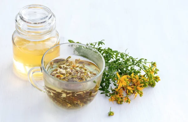 Transparent cup of St. John\'s wort remedy beverage with bunch fresh Hypericum yellow flowers. jar of spring honey. Medicinal herbs for Alternative Medicine and Homeopathic Remedies