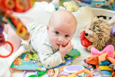 Yeni doğmuş şirin bir kız bebekler için renkli oyuncakların arasında bir yatakta yatıyor. Duyusal gelişim için ilk eğitici oyuncaklar.
