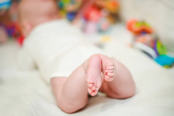 Tiny legs of a baby in a white bodysuit. An admiring innocent girl lying in a comfortable crib in the bedroom. Defocused