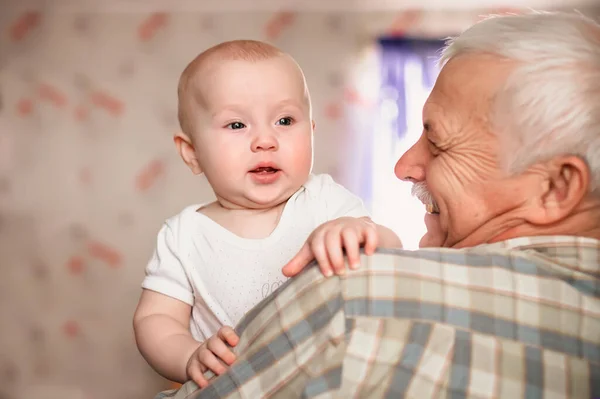 stock image A 3-month-old baby smiles funny. Over shoulder close up of grandfather holding his baby grandson..