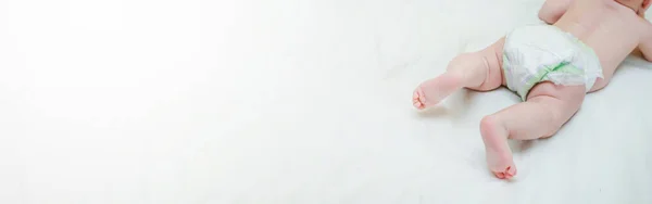 The legs of a newborn baby. Baby pink baby legs that learn to crawl in a crib with a white sheet. a tiny unrecognizable girl moves in a crib. Defocused