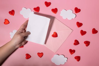 Hand holding a blank letter form for Valentines Day or Mothers Day over an envelope with hearts. Mockup clipart