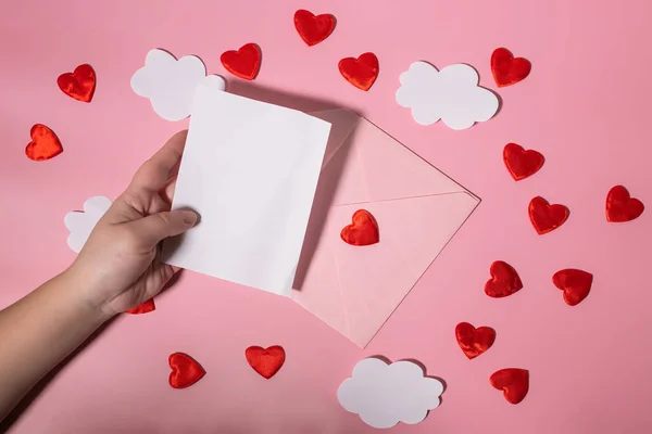 stock image Hand holding a blank letter form for Valentines Day or Mothers Day over an envelope with hearts. Mockup