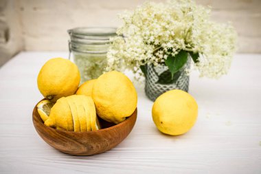 Elderberry fresh flowers picked for the preparation of a refreshing summer drink with lemon. Eco plate with yellow ugly organic lemons on the table