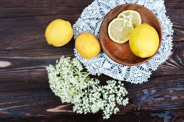 Still life of fresh lemons and elderberry flowers. Ingredients for lemonade and juice from syrup from elderberry flowers. Seasonal summer food. Healing with a healthy diet with ambucus medicines.