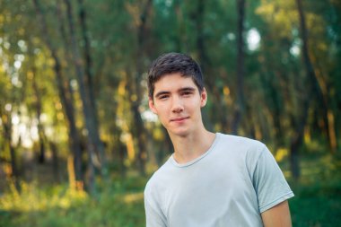 The boy is leaning to one side. The young man smiles. Man walking in the forest at sunset.