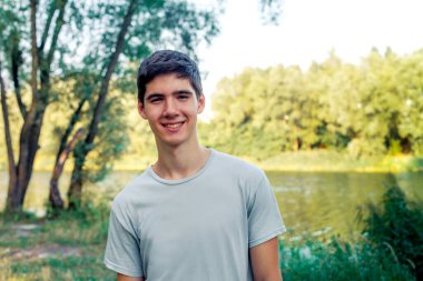 A young man with black hair smiling. Portrait of a gay in nature. Sunny sunset behind the man.