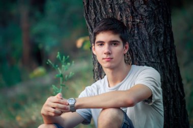 A young man with black hair smiling. Portrait of a gay in nature. Sunny sunset behind the man.