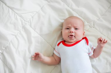 A small newborn baby lies on a white blanket. A child in white with a red bodysuit. Caring for babies up to 2 months.