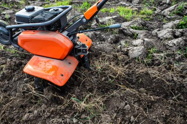 Orange professional cultivator or tiller on untreated soil before plowing. Treatment of virgin land before planting seedlings.