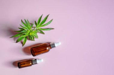 Cannabis on a pink background. Elixir and hemp oil in cosmetic jars with a dispenser.Copy space.
