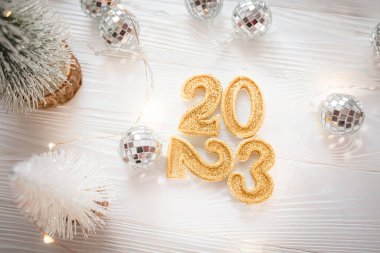Gold numbers 2023 on a white background near disco balls and Christmas trees. 2023 is coming in winter. Light background for the new year.