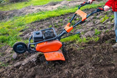 Orange professional cultivator or tiller on untreated soil before plowing. Treatment of virgin land before planting seedlings.