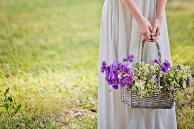 Girl with a basket of flowers. Chrysanthemums and daisies in a basket. Romantic background.