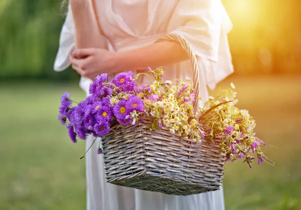 Girl with a basket of flowers. Chrysanthemums and daisies in a basket. Romantic background.