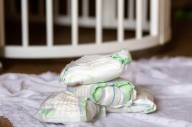 A bunch of dirty used diapers on the floor near the crib. Discarded diapers without a bucket in the nursery.