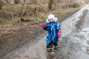 A small child runs along the road with water running through dirty puddles
