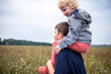 Little sister on her brother's shoulders for a walk in the evening in the countryside in nature