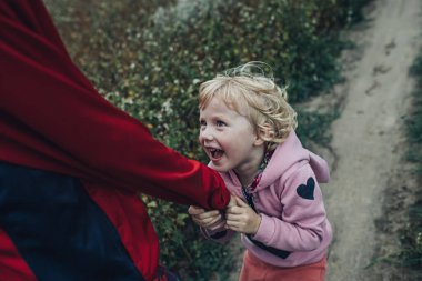 A little girl pulls her brother's sleeve while walking in nature. A happy child plays with his family in the fresh air.