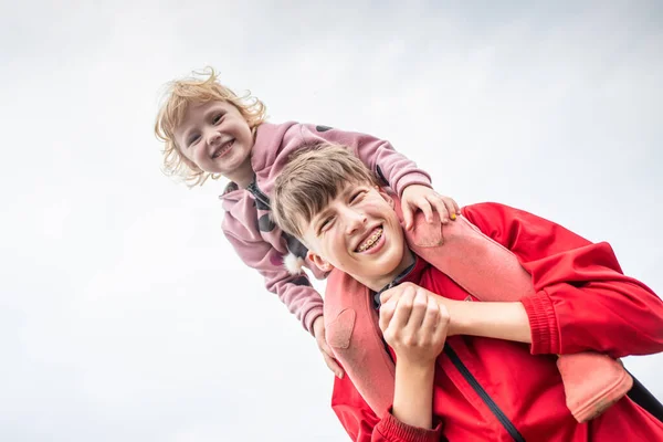 A little girl on her older brother\'s shoulders. Happy children on a walk. The teenage guy smiles sincerely. A teenager has braces on his teeth