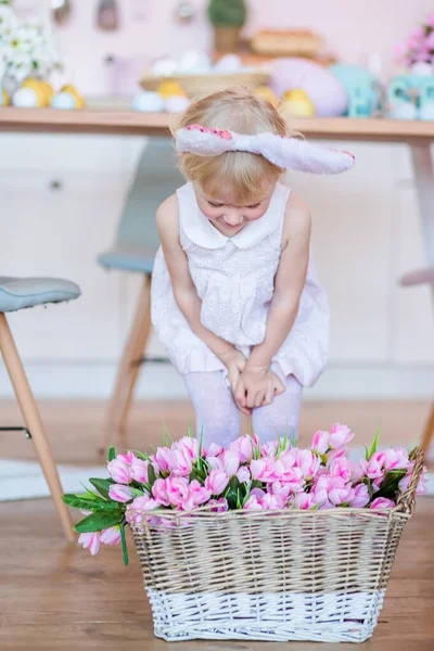 stock image cute little girl stands by basket with spring flowers wearing Easter bunny. Celebration of Easter