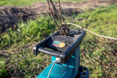 Bahar temizliği sırasında ağaç dallarını parçalamak için elektrikli bahçe öğütücüsü. Ağaçları budadıktan sonra bahçedeki bir yığın kuru dalın karşısında..