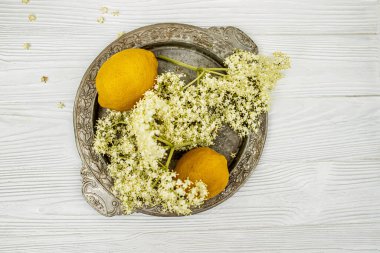 Yazlık terasta şeffaf bir bardak, bir dilim limon ve bir buket mürver. Ambucus şurubuyla sulu içecek. Çiçek açan bir ağaçtan tıbbi bir ürün.