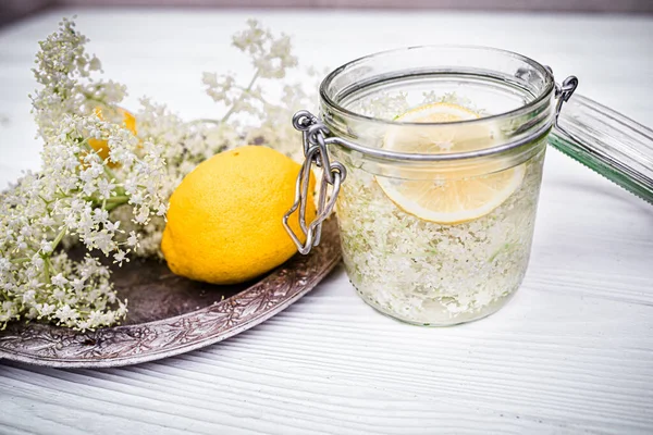 wooden plate with fresh lemons for a healthy refreshing non-alcoholic lemonade with syrup from elderflower flowers. Still life with freshly cut ambucus flowers in a jar