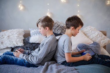 İki çocuk sırtüstü oturup telefonlarıyla duvardaki Noel ışıklarına karşı oyunlar oynuyor.