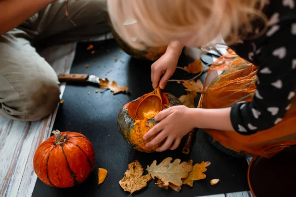 Kids in costume delight in pumpkin carving, a Halloween tradition.