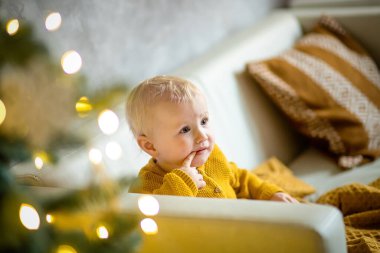 Kürk ağacının önünde ağzında altın dekoru olan küçük bir kız. Şaşırmış kız. Yeni yıl arifesi. Noel arifesi. Kürk ağacı konseptinde rahat bir tatil.