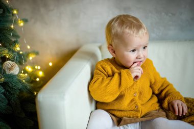 Kürk ağacının önünde ağzında altın dekoru olan küçük bir kız. Şaşırmış kız. Yeni yıl arifesi. Noel arifesi. Kürk ağacı konseptinde rahat bir tatil.