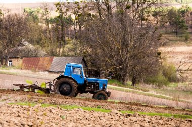 Tarlada saban süren ve toprak eken eski mavi traktör. Baharda toprağı sebze ekmeye hazırlıyorum. Tarım makineleri, saha çalışması.