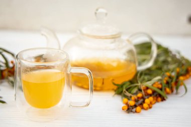 Şeffaf bir çaydanlığın yanında aromatik deniz karabatağı çayıyla dolu berrak cam bardak. Vitamin zengini deniz dikenli karabatak çayı, sağlık için doğal bir ilaç.