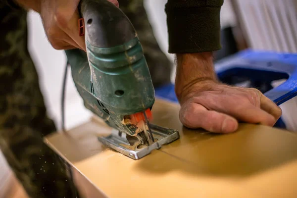 carpenters hand using an electric jigsaw to cut wooden plywood. The plywood is cut into a precise shape, and the carpenters hand is steady and confident.