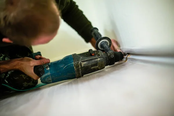 Man drilling a hole in the wall with a drill bit. Using an electric drill to install skirting boards