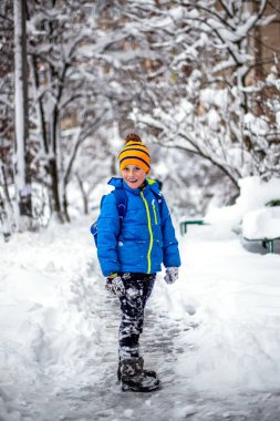 Erkek öğrenci kışın karlı yolda sırt çantasıyla yürüyor.