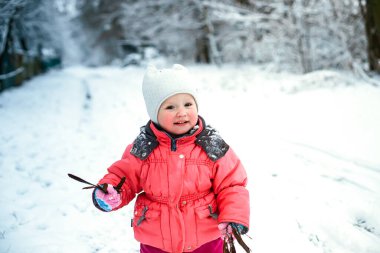 Kış tulumu giymiş komik küçük bir kız kar yağışı sırasında ellerini kış manzarasının arka planına kaldırdı. Bağışıklık sistemi güçleniyor.