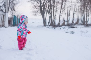 Kışın karlı sokakta duran parlak kışlık takım elbiseli küçük kız.