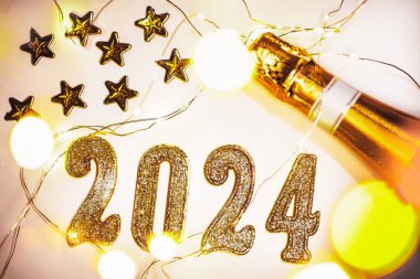 Yeni yıl 2024. Şenlikli arka plan, köpüklü şarap şişesi ve beyaz arka planda altın numaralarla aydınlık ve bokeh..