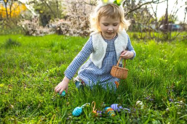 Paskalya yumurtası avı. Elinde sepetlerle parkta renkli yumurta toplayan küçük bir kız.
