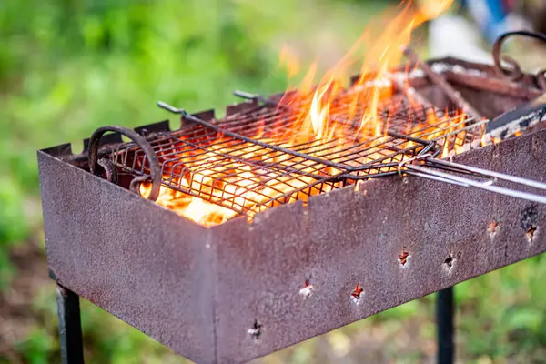 A large metal grill filled with burning wood and an old rusty grill grate