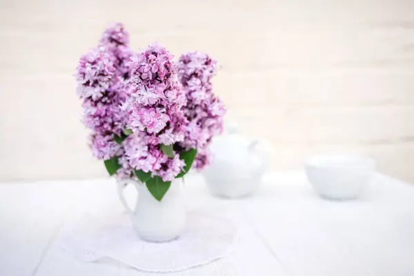 Bouquet of lilacs in a white vase on a served table. Fresh lilac flowers in spring for tea party decor.