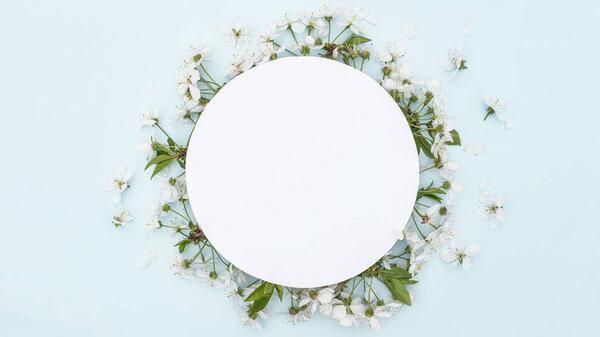 Round frame with spring cherry flowers. Flowers on cherry tree branches in form of wreath on blue background. Leaf pattern. Flat lay, top view, copy space. Mockup.