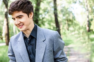 Şehir parkında kameraya bakmayan gülümseyen bir gencin ön portresi. Genç yaşam tarzı konsepti.