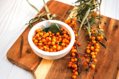 Taze toplanmış deniz dikenli üzümler beyaz tabakta ve kesme tahtasındaki deniz dikenli dallar..