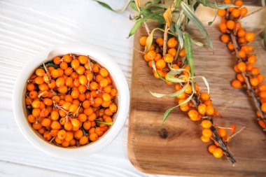 Beyaz tabakta taze toplanmış deniz dikenli üzümler ve masada deniz dikenli diken dalları. Üst görünüm. 